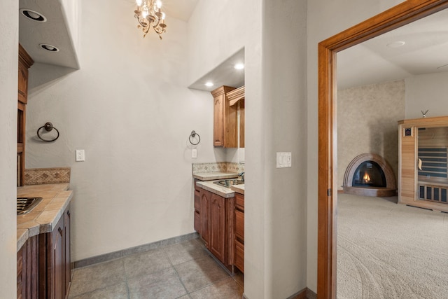 2632 Globe Ct NE, Rio Rancho, NM 87124 - kitchen with tile countertops, a glass covered fireplace, brown cabinets, light tile patterned floors, and a chandelier