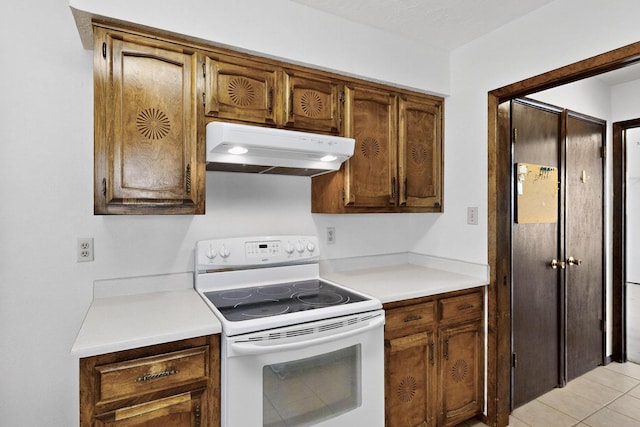 5207 Russell Dr NW, Albuquerque, NM 87114 - kitchen with white range with electric stovetop, under cabinet range hood, light countertops, light tile patterned floors, and brown cabinetry