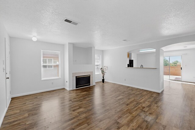 7408 Estes Park Ave NW, Albuquerque, NM 87114 - unfurnished living room featuring a textured ceiling, dark wood-type flooring, a fireplace, and arched walkways