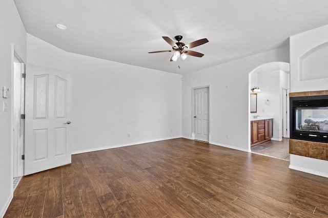 1128 San Augustin Dr, Bernalillo, NM 87004 - unfurnished living room with a ceiling fan, dark wood-type flooring, arched walkways, and a tile fireplace
