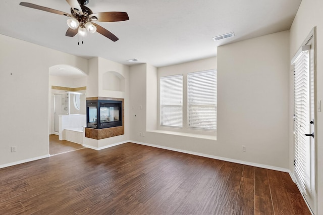 1128 San Augustin Dr, Bernalillo, NM 87004 - unfurnished living room with ceiling fan, wood finished floors, a multi sided fireplace, and arched walkways
