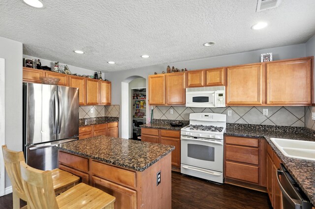 1230 Carrizo St NW, Los Lunas, NM 87031 - kitchen featuring stainless steel appliances, arched walkways, a kitchen island, dark wood-style floors, and backsplash