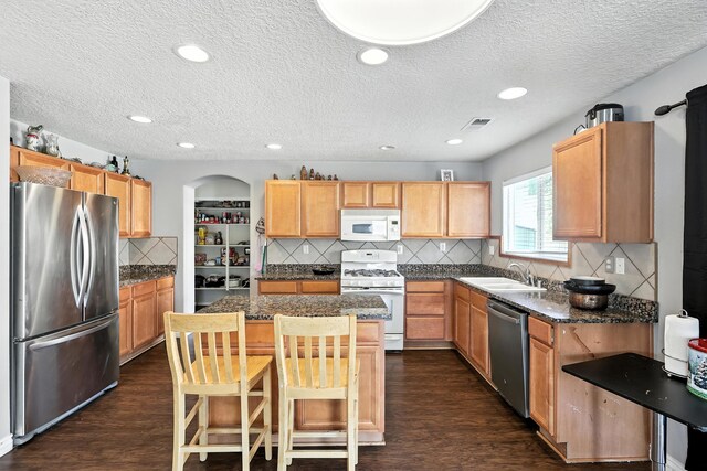 1230 Carrizo St NW, Los Lunas, NM 87031 - kitchen with appliances with stainless steel finishes, dark wood-style floors, a textured ceiling, a center island, and decorative backsplash