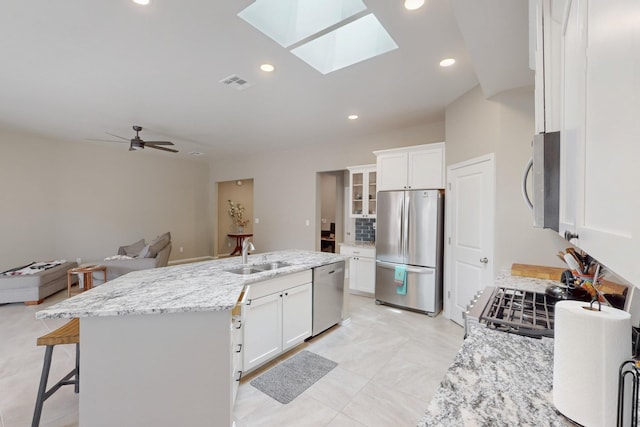 4813 Guadalupe Peak St SW, Los Lunas, NM 87031 - kitchen featuring stainless steel appliances, white cabinetry, a center island with sink, light stone countertops, and a skylight