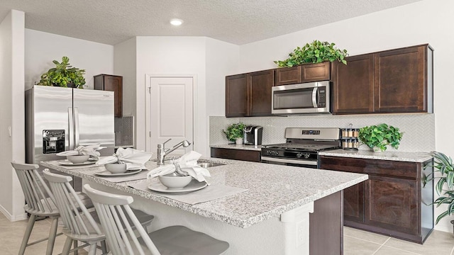 5627 Sagan Loop SE, Albuquerque, NM 87106 - kitchen featuring appliances with stainless steel finishes, a kitchen breakfast bar, dark brown cabinets, a center island with sink, and light countertops