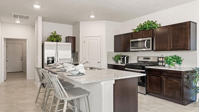 5627 Sagan Loop SE, Albuquerque, NM 87106 - kitchen featuring stainless steel appliances, a breakfast bar area, dark brown cabinets, an island with sink, and decorative backsplash