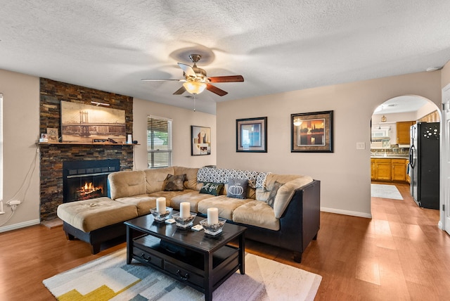 6404 Gambel Quail Rd NE, Rio Rancho, NM 87144 - living area with a ceiling fan, light wood-style floors, a textured ceiling, a stone fireplace, and arched walkways