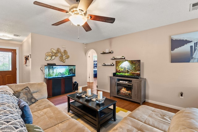 6404 Gambel Quail Rd NE, Rio Rancho, NM 87144 - living area with arched walkways, wood finished floors, ceiling fan, a warm lit fireplace, and a textured ceiling