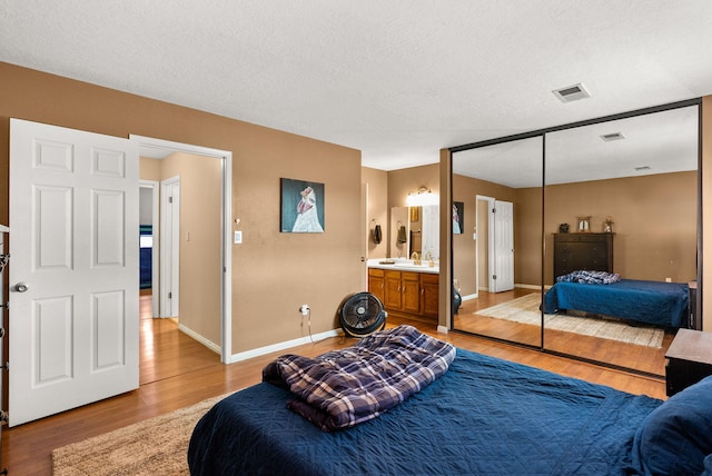 6404 Gambel Quail Rd NE, Rio Rancho, NM 87144 - bedroom featuring light wood-type flooring, connected bathroom, a closet, and a textured ceiling