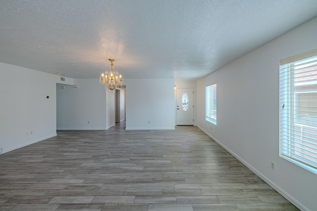 3742 Cattle Dr NE, Rio Rancho, NM 87144 - unfurnished living room with a chandelier, a textured ceiling, plenty of natural light, and light wood-type flooring