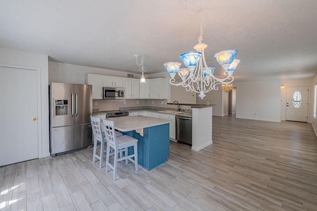 3742 Cattle Dr NE, Rio Rancho, NM 87144 - kitchen featuring appliances with stainless steel finishes, a chandelier, white cabinets, a kitchen island, and light wood-style floors