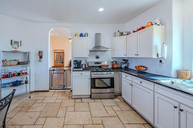 300 Thompson, Moriarty, NM 87035 - kitchen with wall chimney range hood, stainless steel gas range oven, arched walkways, dark countertops, and white cabinets