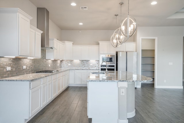 205 Silent Spring Dr NE, Rio Rancho, NM 87124 - kitchen with stainless steel appliances, wood finished floors, wall chimney exhaust hood, an island with sink, and backsplash
