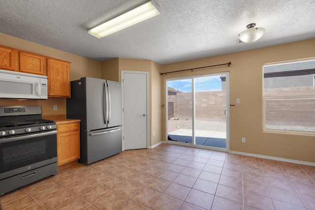 1944 Sierra Norte Loop NE, Rio Rancho, NM 87144 - kitchen with appliances with stainless steel finishes, a textured ceiling, light tile patterned floors, brown cabinetry, and light countertops