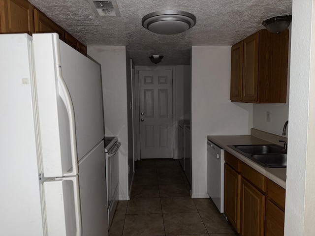 8333 Comanche Rd NE Unit 10B, Albuquerque, NM 87110 - kitchen featuring white appliances, tile patterned floors, washing machine and dryer, brown cabinetry, and a textured ceiling
