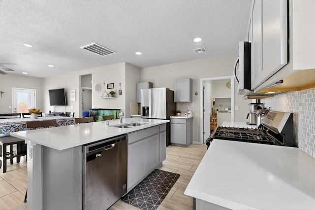 4823 Blackburn Rd NE, Rio Rancho, NM 87144 - kitchen featuring appliances with stainless steel finishes, gray cabinetry, light countertops, a kitchen island with sink, and a textured ceiling