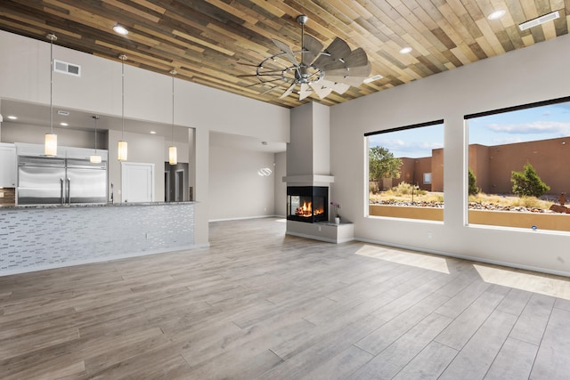 7 Aztec Ct, Placitas, NM 87043 - unfurnished living room featuring ceiling fan, wood finished floors, a towering ceiling, a multi sided fireplace, and wood ceiling