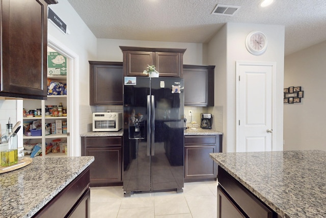 1854 Valle Vista Rd NW, Los Lunas, NM 87031 - kitchen with black refrigerator with ice dispenser, backsplash, light stone countertops, dark brown cabinetry, and a textured ceiling