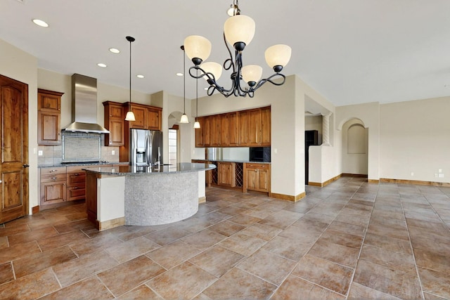 2413 Desert View Rd NE, Rio Rancho, NM 87144 - kitchen with wall chimney range hood, stainless steel fridge, brown cabinets, backsplash, and a kitchen island with sink