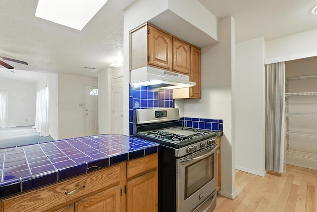 6205 Darlene Pl SW, Albuquerque, NM 87105 - kitchen with gas range, under cabinet range hood, tile counters, ceiling fan, and light wood-type flooring