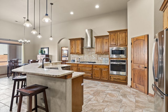 9844 Cameron St NW, Albuquerque, NM 87114 - kitchen featuring stainless steel appliances, wall chimney exhaust hood, brown cabinets, a towering ceiling, and a breakfast bar area