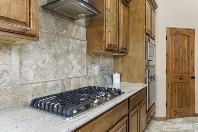 9844 Cameron St NW, Albuquerque, NM 87114 - kitchen with wall chimney range hood, stainless steel appliances, decorative backsplash, and brown cabinets