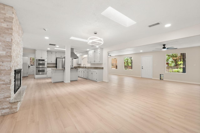 697 W W Meadowlark Ln, Corrales, NM 87048 - unfurnished living room with a stone fireplace, a skylight, recessed lighting, light wood finished floors, and a ceiling fan