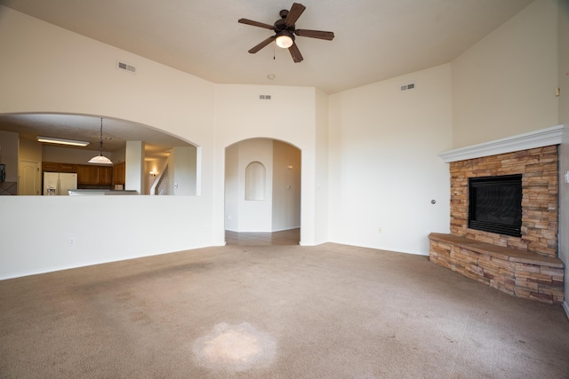 5485 Roosevelt Loop NE, Rio Rancho, NM 87144 - unfurnished living room featuring a ceiling fan, carpet flooring, a stone fireplace, and arched walkways