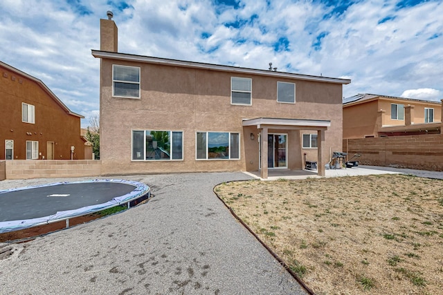 1191 Carrizo St NW, Los Lunas, NM 87031 - rear view of house with a trampoline, a patio, a fenced backyard, stucco siding, and a chimney