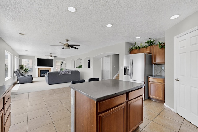 1191 Carrizo St NW, Los Lunas, NM 87031 - kitchen featuring stainless steel fridge, light tile patterned flooring, brown cabinets, dark countertops, and arched walkways