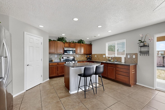 1191 Carrizo St NW, Los Lunas, NM 87031 - kitchen with appliances with stainless steel finishes, a breakfast bar, brown cabinets, backsplash, and recessed lighting