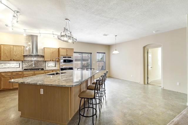 1852 Smarty Jones St SE, Albuquerque, NM 87123 - kitchen featuring wall chimney range hood, stainless steel appliances, tasteful backsplash, a kitchen island with sink, and arched walkways