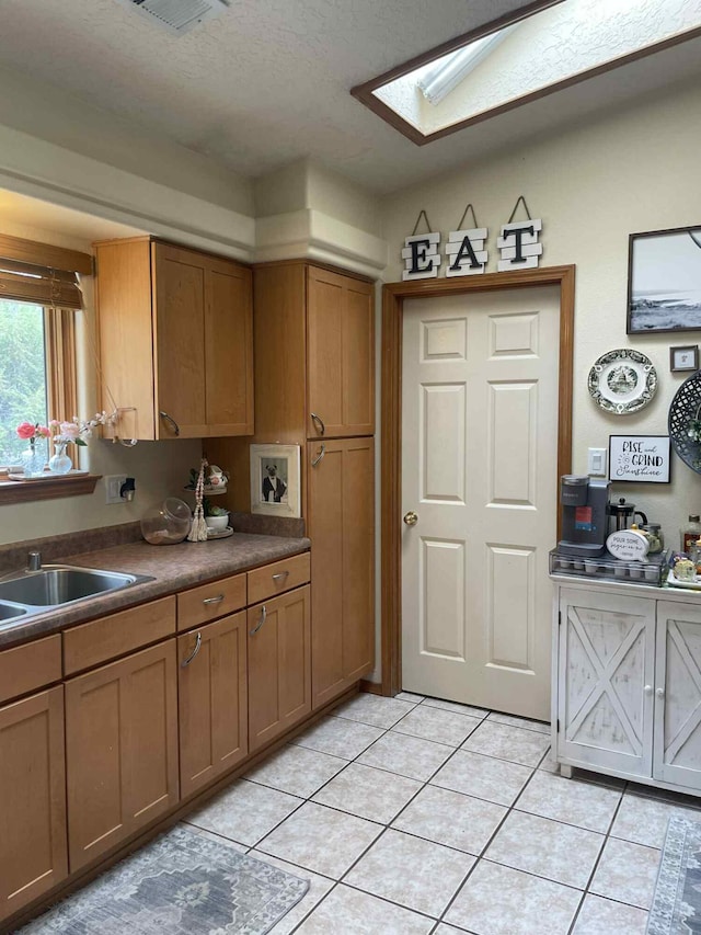 34358 US Highway 285, Ojo Caliente, NM 87549 - kitchen with light tile patterned floors, a skylight, brown cabinets, and dark countertops
