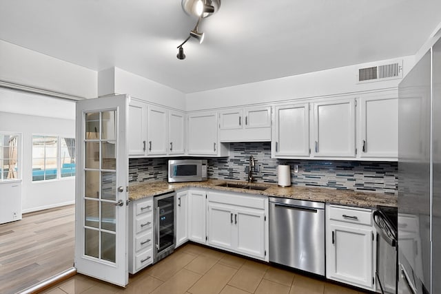 1308 Boatright Dr NE, Albuquerque, NM 87112 - kitchen featuring appliances with stainless steel finishes, wine cooler, white cabinets, tasteful backsplash, and light stone countertops