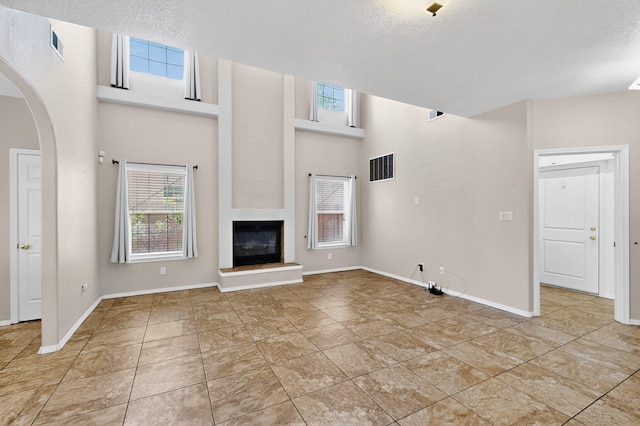 5508 Carefree Ave NW, Albuquerque, NM 87120 - unfurnished living room featuring a glass covered fireplace, arched walkways, a textured ceiling, light tile patterned floors, and a towering ceiling