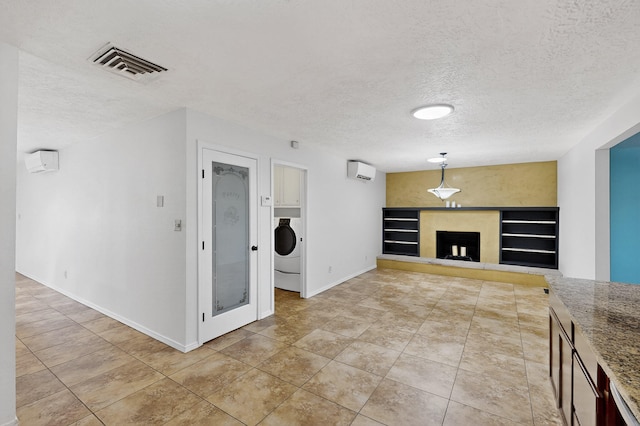12208 Phoenix Ave NE, Albuquerque, NM 87112 - unfurnished living room with a textured ceiling, a fireplace with raised hearth, a wall mounted air conditioner, light tile patterned floors, and washer / clothes dryer