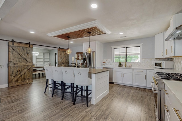 4320 Blumenshine Cir SW, Albuquerque, NM 87105 - kitchen featuring a barn door, appliances with stainless steel finishes, a breakfast bar, wood finished floors, and decorative backsplash