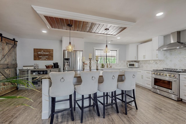 4320 Blumenshine Cir SW, Albuquerque, NM 87105 - kitchen featuring wall chimney exhaust hood, appliances with stainless steel finishes, a barn door, backsplash, and white cabinetry