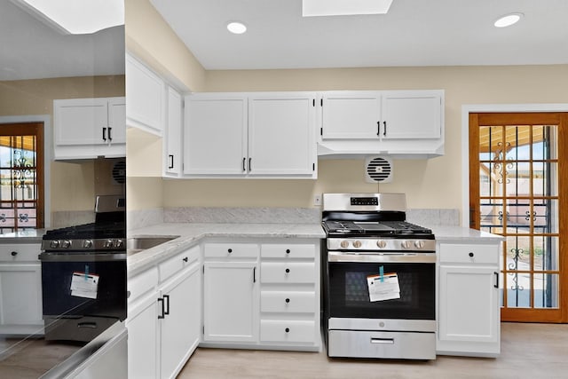 10409 Britt Ct NE, Albuquerque, NM 87112 - kitchen featuring stainless steel gas range oven, white cabinetry, light wood finished floors, recessed lighting, and light stone countertops