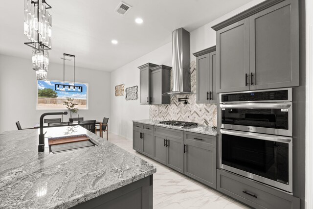 1109 11th St SE, Rio Rancho, NM 87124 - kitchen with appliances with stainless steel finishes, gray cabinetry, a chandelier, tasteful backsplash, and wall chimney exhaust hood