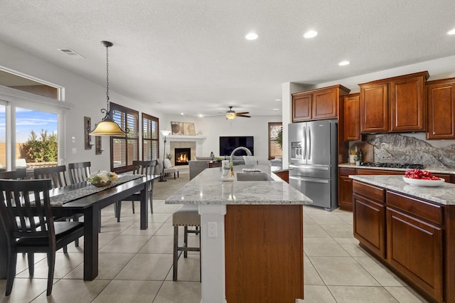 44 Los Balcones Pl NE, Rio Rancho, NM 87124 - kitchen featuring stainless steel refrigerator with ice dispenser, a tile fireplace, an island with sink, ceiling fan, and gas stovetop