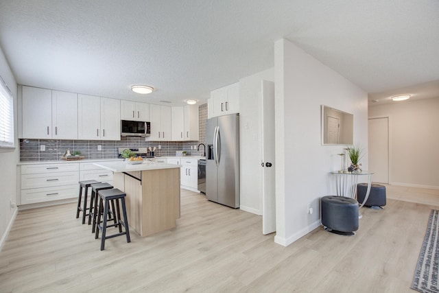 4920 Black Dr NW, Albuquerque, NM 87120 - kitchen featuring appliances with stainless steel finishes, a kitchen breakfast bar, a kitchen island, light wood-style flooring, and light countertops