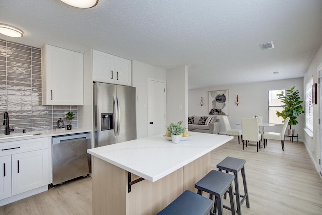 4920 Black Dr NW, Albuquerque, NM 87120 - kitchen with stainless steel appliances, a kitchen breakfast bar, light wood-type flooring, decorative backsplash, and a textured ceiling