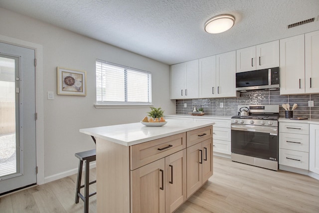 4920 Black Dr NW, Albuquerque, NM 87120 - kitchen featuring appliances with stainless steel finishes, a kitchen bar, tasteful backsplash, light wood-style floors, and light countertops