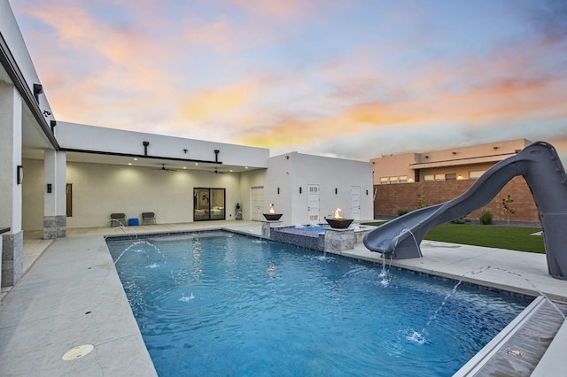 7900 Aguila St NW, Albuquerque, NM 87120 - pool at dusk featuring a water slide, an outdoor pool, ceiling fan, and a patio area