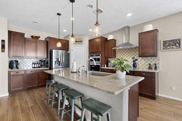 6417 Kings Cyn NE, Rio Rancho, NM 87144 - kitchen with appliances with stainless steel finishes, wall chimney range hood, light wood-type flooring, a breakfast bar area, and backsplash