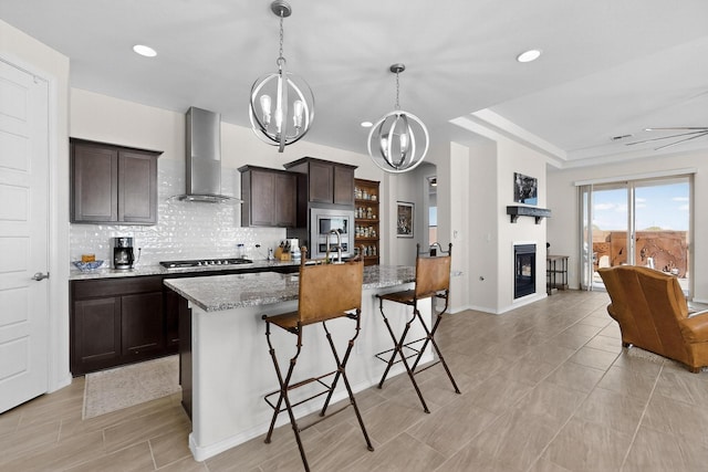 4293 Crowned Eagle Loop NE, Rio Rancho, NM 87144 - kitchen featuring wall chimney range hood, dark brown cabinets, decorative backsplash, a kitchen bar, and a center island with sink