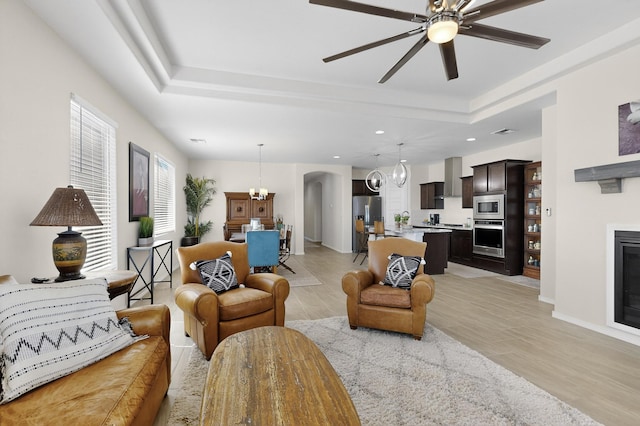 4293 Crowned Eagle Loop NE, Rio Rancho, NM 87144 - living room with a raised ceiling, a fireplace, light wood-style flooring, a chandelier, and a ceiling fan