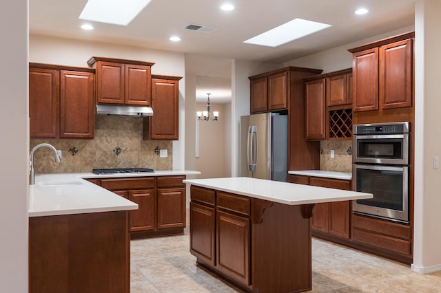 959 Salt Cedar Ct, Bernalillo, NM 87004 - kitchen with stainless steel appliances, a skylight, under cabinet range hood, decorative backsplash, and a center island