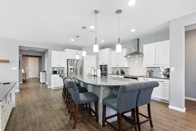 9015 Vista Dibujo Rd, Albuquerque, NM 87120 - kitchen with wall chimney range hood, appliances with stainless steel finishes, a kitchen bar, dark wood finished floors, and decorative backsplash